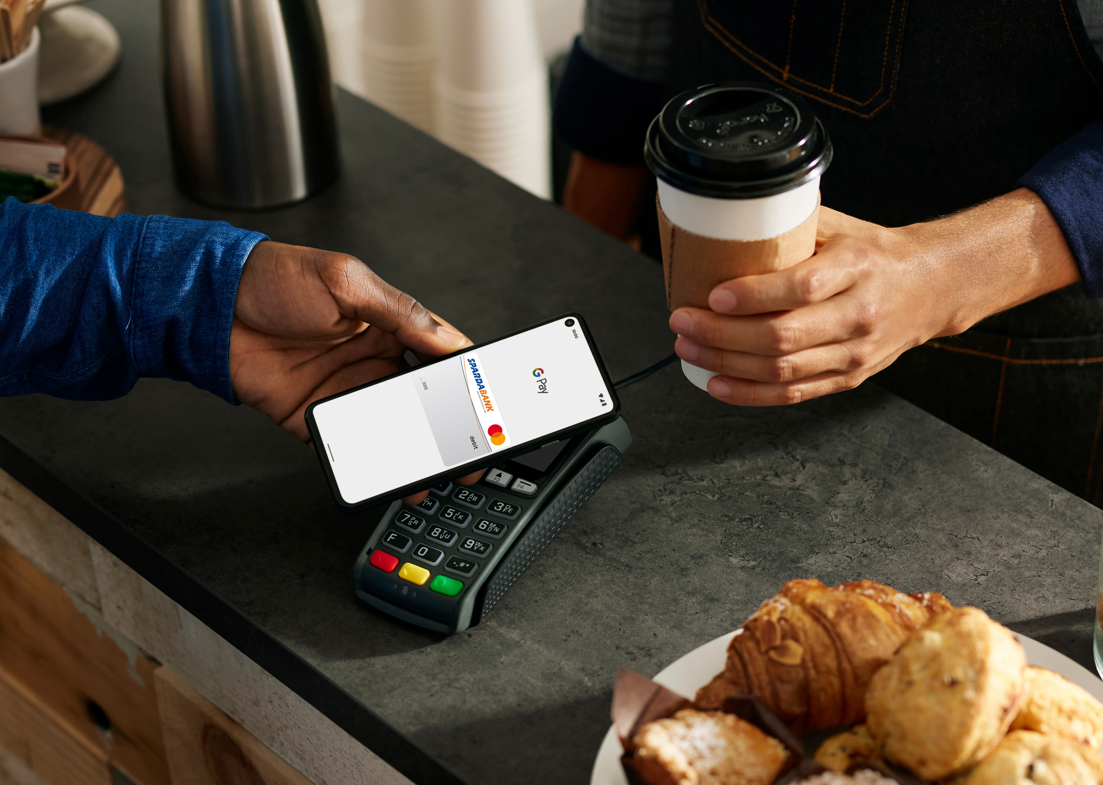 Ein Mann zahlt mit Smartphone Google Pay und Volksbank Mastercard in einem Café.