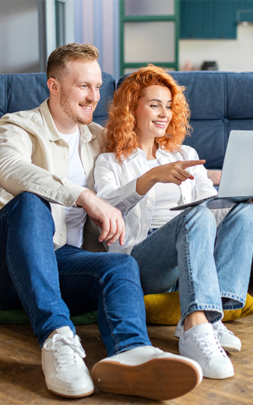 Zwei Personen sitzen auf einem Sofa und nutzen gemeinsam einen Laptop. Eine Person zeigt auf den Bildschirm.