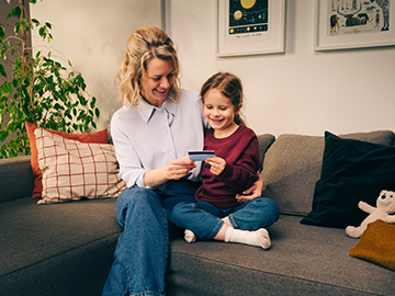 Eine Mutter liegt auf der Couch und stemmt spielerisch ihren jungen Sohn mit den Füßen in die Höhe. Beide lachen