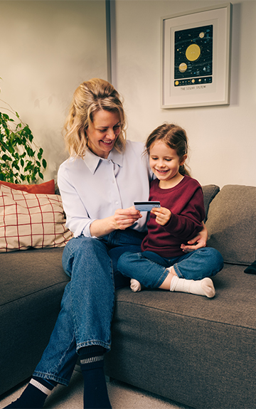 Eine Mutter sitzt mit ihrem Kind auf der Couch, beide halten eine Spar-Karte in der Hand und betrachten diese.