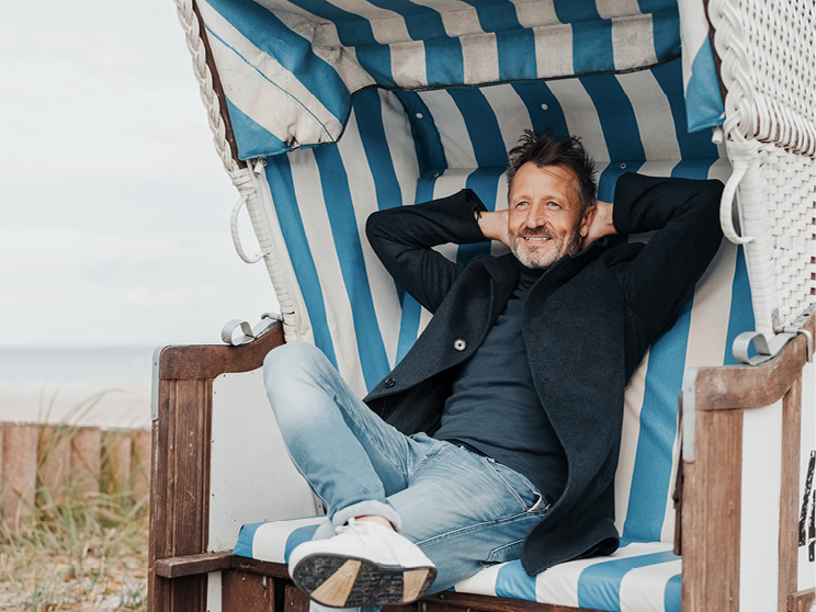 Eine Person genießt einen entspannten Moment im Strandkorb am Meer. Das Motiv steht für Gelassenheit, Sicherheit und einen sorgenfreien Blick auf die Zukunft.