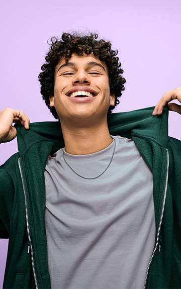 Ein junger Mann mit dunklen Locken tanzt vor lila Hintergrund.