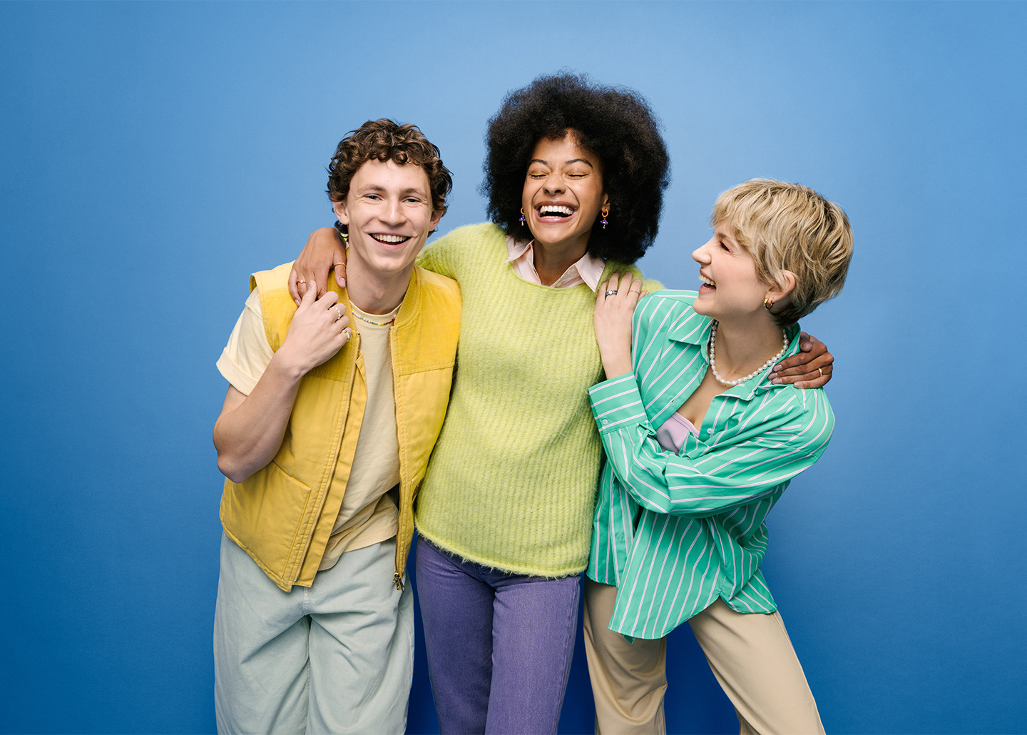 Drei Freunde, zwei Mädchen und ein Junge umarmen sich und lachen.