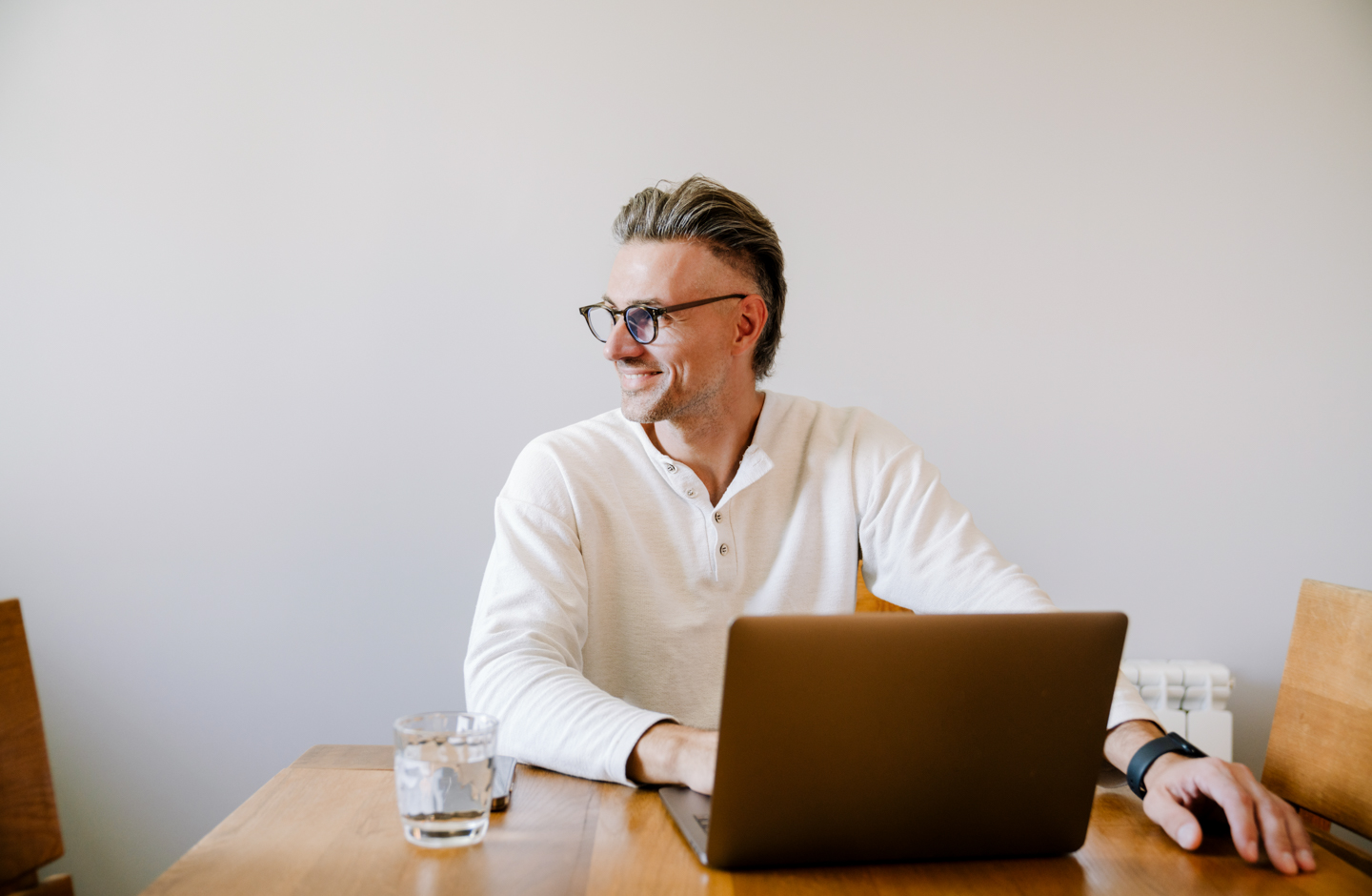 Mann sitzt vor dem Laptop und blickt fröhlich nach rechts.