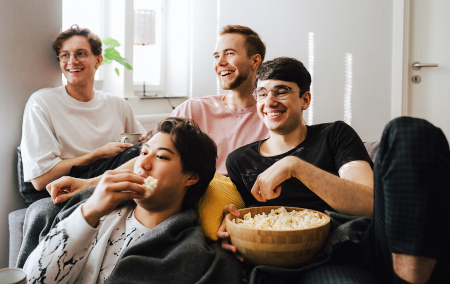 Vier Jugendliche sitzen auf einer Couch, lachen und essen Popcorn